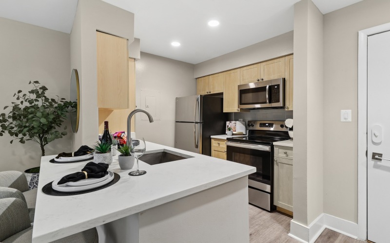Large well lit kitchen with white granite countertops, wood floors and stainless steel appliances.